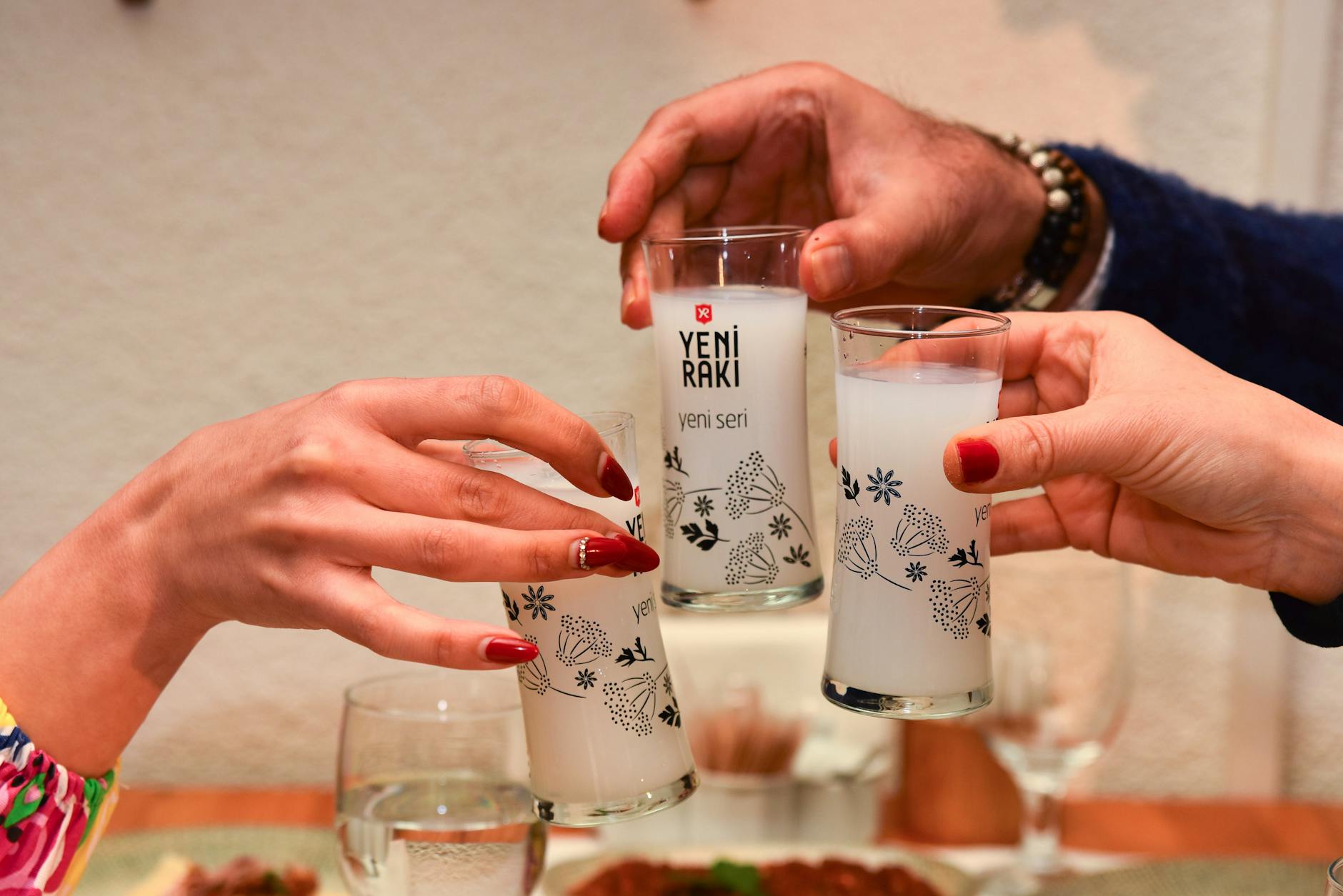 Trois personnes trinquant avec des verres de rakı opaques lors d'un repas convivial.