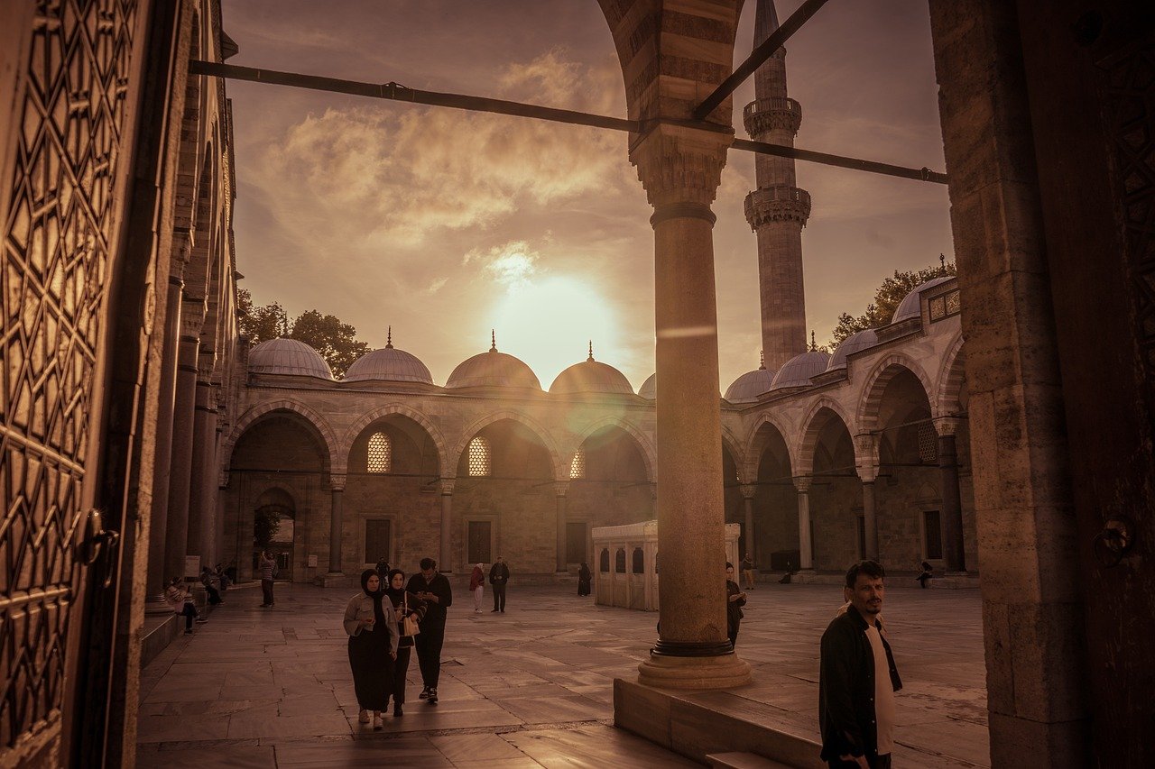 Cour intérieure majestueuse d'une mosquée ottomane à Istanbul, capturée au coucher du soleil. Les arcades et les dômes sont illuminés par une lumière dorée éclatante, rappelant l'atmosphère d'une longue marche solitaire à travers l'histoire de la ville, loin des Murailles de Théodose.