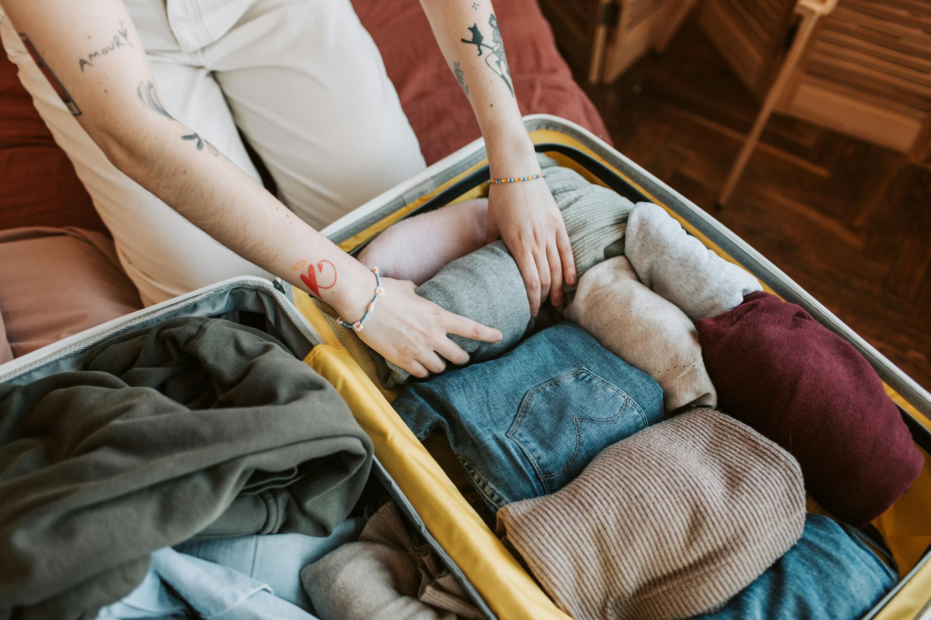 Une personne range soigneusement des vêtements d'hiver pliés dans une valise ouverte sur un lit.