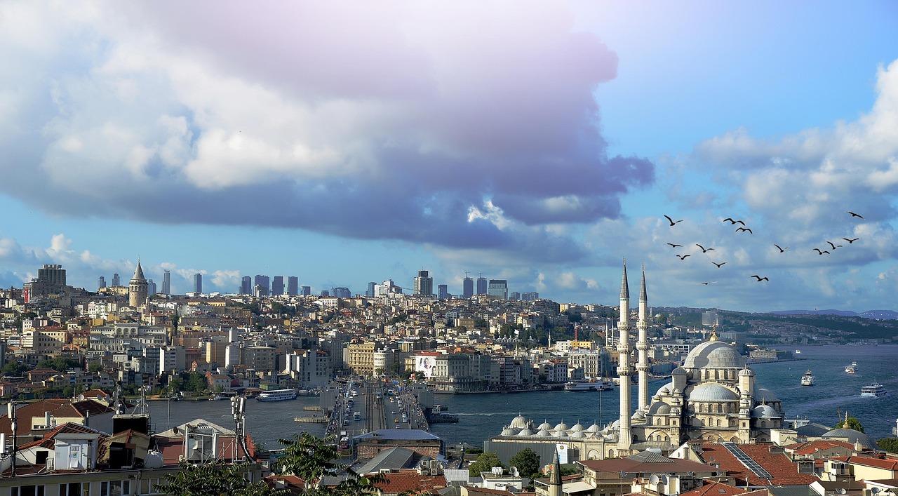 Vue panoramique impressionnante sur la Corne d'Or à Istanbul, encadrant la Mosquée de Yeni Cami au premier plan avec ses dômes et minarets sous un ciel nuageux dramatique. À l'arrière-plan, on distingue la silhouette historique de la ville avec la Tour de Galata et les gratte-ciel modernes, rappelant le décor d'une longue marche solitaire le long des murs anciens de Théodose.