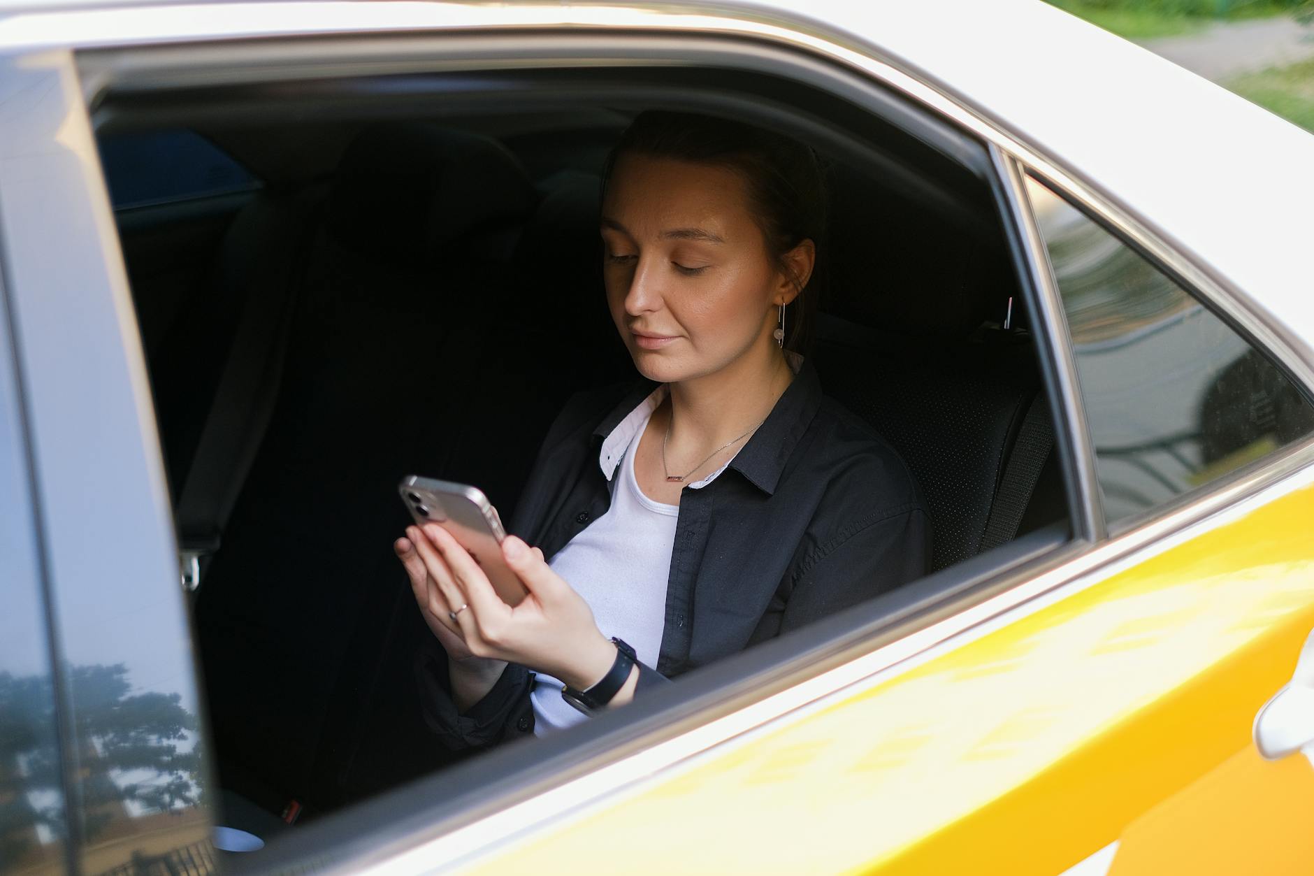 Une femme consulte son téléphone portable à l'arrière d'un taxi jaune en ville.
